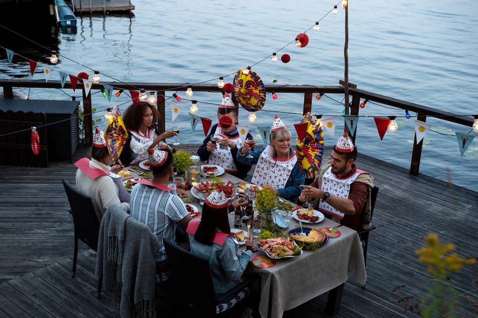 Guests raising glasses around a dockside Kräftskiva table under string lights